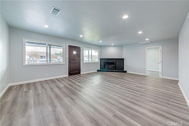 unfurnished living room with a brick fireplace and light hardwood / wood-style flooring