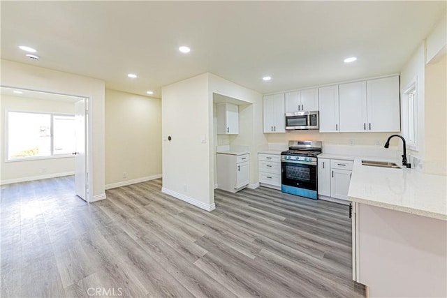 kitchen with sink, light hardwood / wood-style flooring, appliances with stainless steel finishes, light stone countertops, and white cabinets