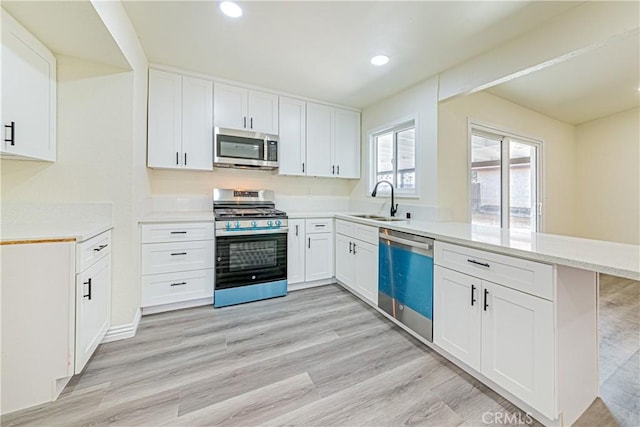 kitchen with appliances with stainless steel finishes, sink, white cabinets, light hardwood / wood-style floors, and kitchen peninsula