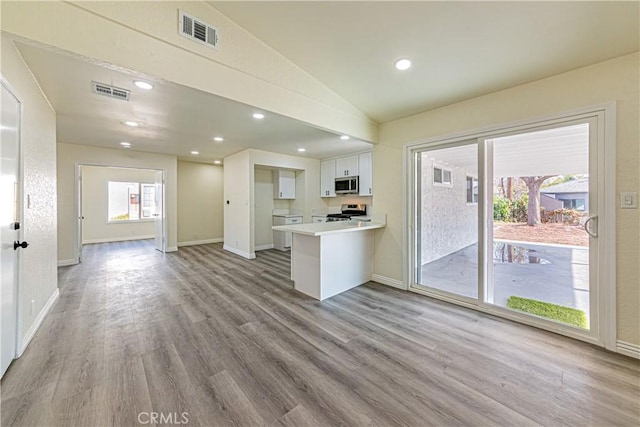 kitchen with vaulted ceiling, kitchen peninsula, stainless steel appliances, light hardwood / wood-style floors, and white cabinets