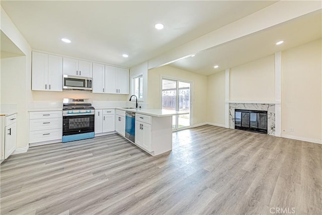 kitchen with sink, kitchen peninsula, stainless steel appliances, a fireplace, and white cabinets