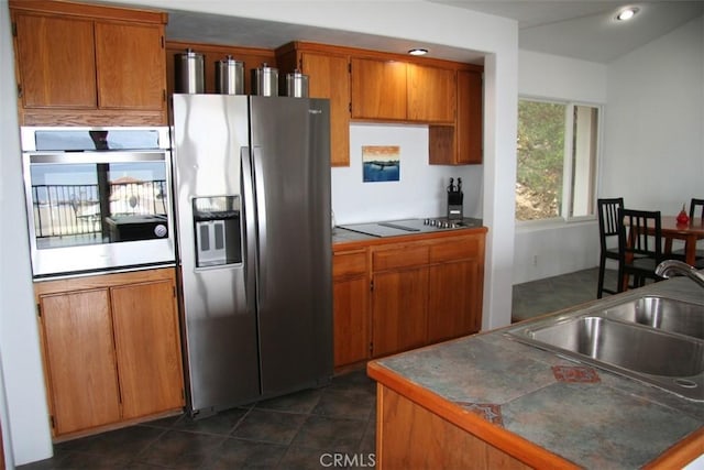 kitchen with appliances with stainless steel finishes, tile counters, dark tile patterned flooring, and sink