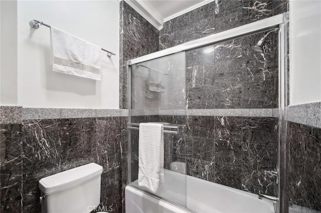 bathroom with tile walls, ornamental molding, toilet, and combined bath / shower with glass door