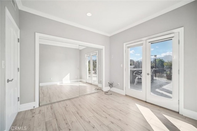 empty room featuring french doors, ornamental molding, and light wood-type flooring