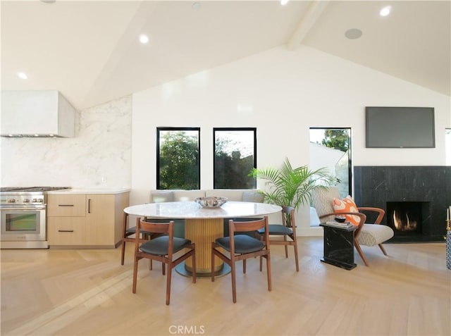 dining space with light parquet floors, high vaulted ceiling, a high end fireplace, and beam ceiling