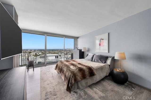 bedroom with hardwood / wood-style floors, access to exterior, and a wall of windows