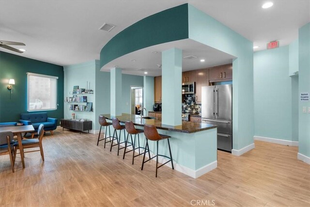 kitchen with light hardwood / wood-style flooring, stainless steel appliances, kitchen peninsula, and a kitchen bar