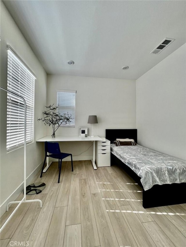 bedroom with multiple windows, built in desk, and light hardwood / wood-style flooring