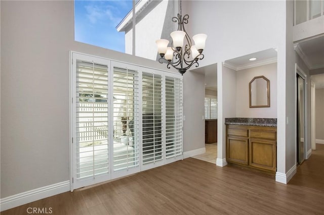 unfurnished dining area with a high ceiling, ornamental molding, an inviting chandelier, and dark hardwood / wood-style flooring