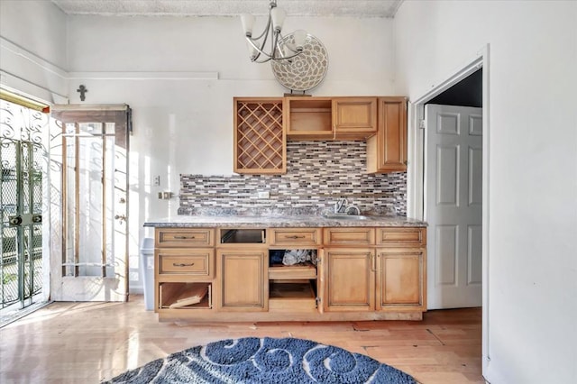 kitchen featuring sink, light hardwood / wood-style flooring, backsplash, light stone countertops, and a chandelier