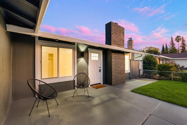 back house at dusk featuring a patio and a yard