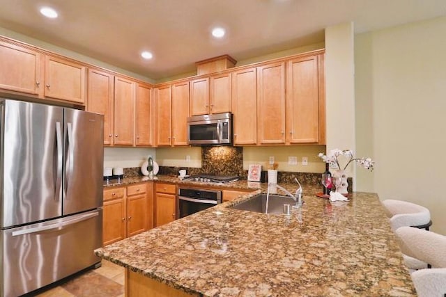 kitchen with a kitchen bar, sink, kitchen peninsula, stone counters, and stainless steel appliances