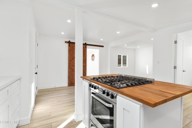 kitchen with light hardwood / wood-style flooring, wooden counters, oven, white cabinets, and a barn door