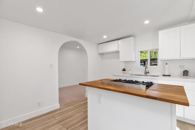 kitchen with stainless steel gas cooktop, sink, butcher block countertops, and white cabinets