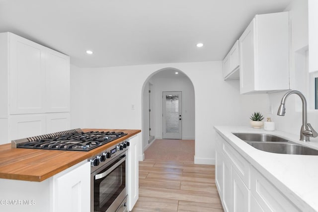 kitchen featuring wood counters, sink, stainless steel range with gas stovetop, light hardwood / wood-style floors, and white cabinets