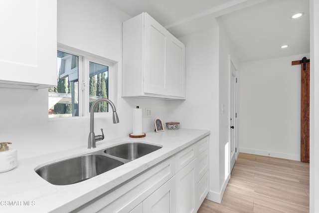 kitchen featuring sink, white cabinetry, light stone counters, light hardwood / wood-style floors, and a barn door