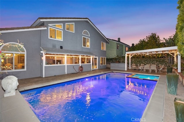 pool at dusk with an in ground hot tub and a patio