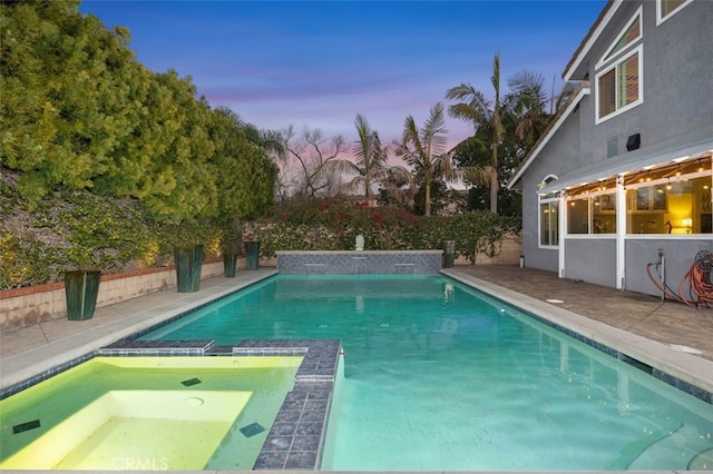 pool at dusk featuring an in ground hot tub