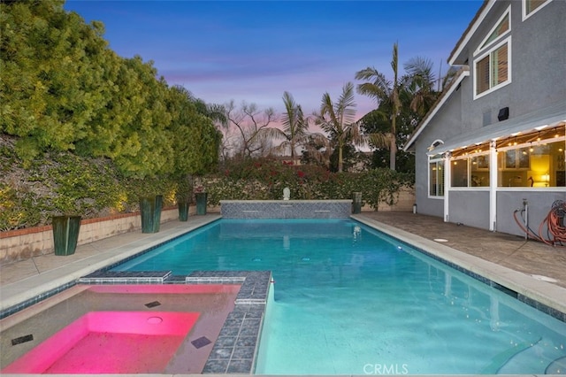 pool at dusk with an in ground hot tub