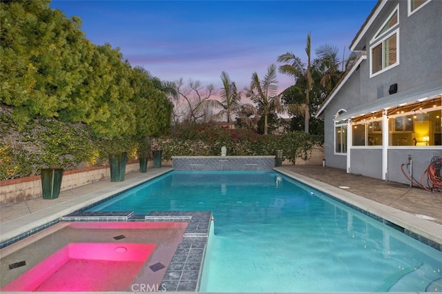 pool at dusk featuring a patio area and a pool with connected hot tub
