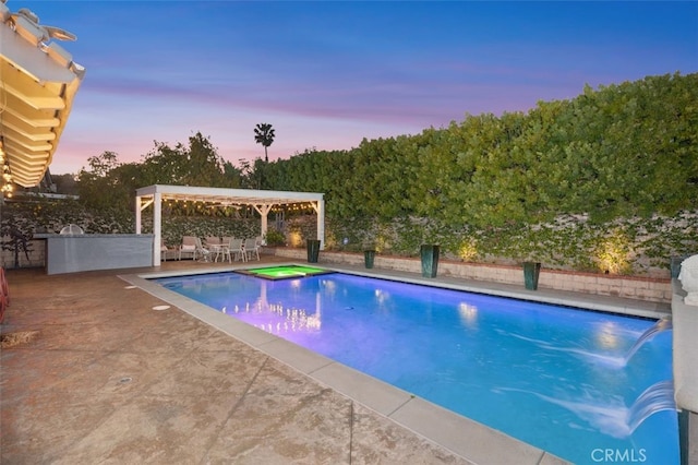 pool at dusk featuring a patio and an in ground hot tub