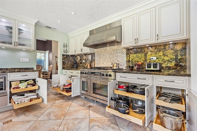 kitchen with white cabinets, wall chimney exhaust hood, double oven range, tasteful backsplash, and visible vents