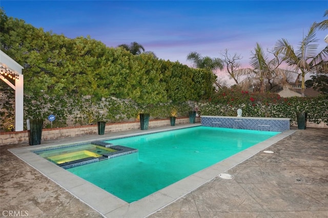 pool at dusk with an in ground hot tub and a patio