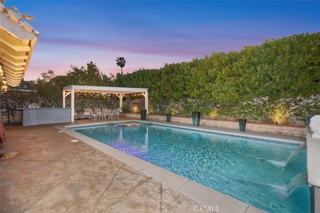 pool at dusk featuring a patio area and an in ground hot tub