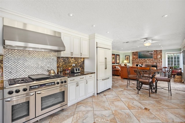 kitchen featuring tasteful backsplash, premium appliances, a fireplace, ornamental molding, and wall chimney exhaust hood