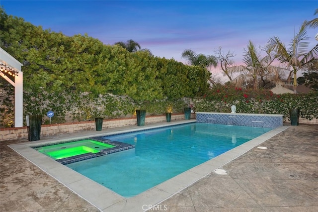 pool at dusk with an in ground hot tub