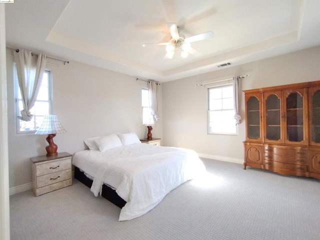 carpeted bedroom featuring multiple windows, a tray ceiling, and ceiling fan