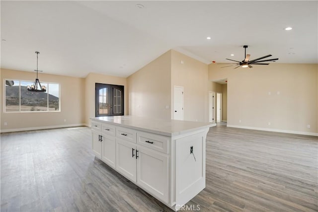 kitchen with vaulted ceiling, a kitchen island, white cabinetry, hanging light fixtures, and hardwood / wood-style flooring