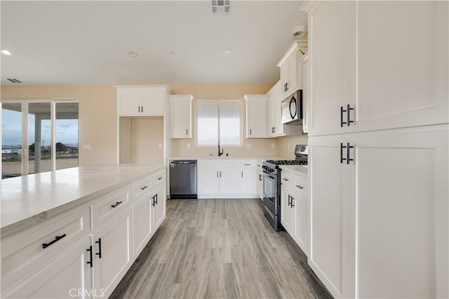 kitchen with sink, light stone counters, stainless steel appliances, light hardwood / wood-style floors, and white cabinets