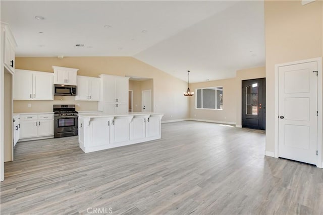 kitchen featuring an island with sink, lofted ceiling, white cabinetry, stainless steel appliances, and an inviting chandelier