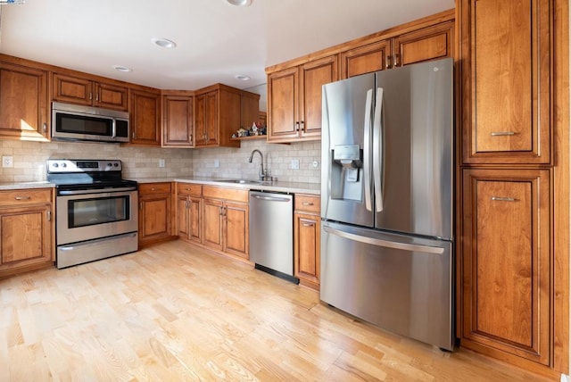 kitchen with stainless steel appliances, sink, backsplash, and light wood-type flooring