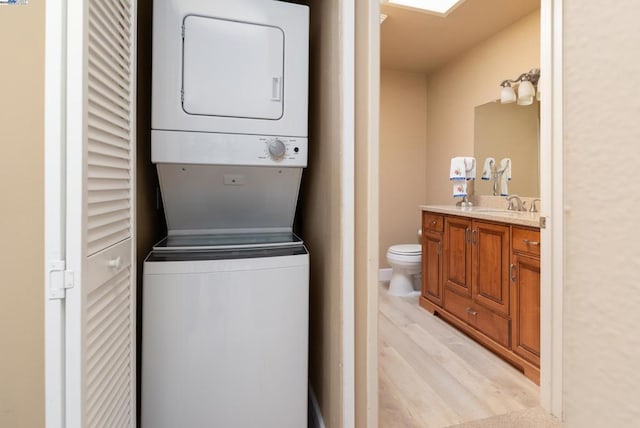 laundry area featuring stacked washer / dryer, sink, and light hardwood / wood-style flooring