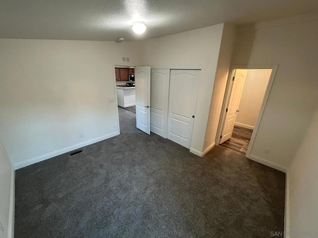 unfurnished bedroom featuring dark colored carpet, a textured ceiling, and a closet