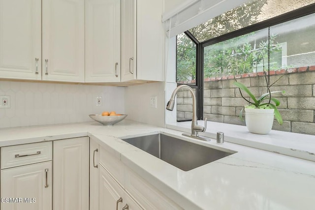 kitchen featuring tasteful backsplash, white cabinetry, sink, and light stone counters