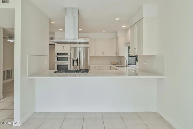 kitchen featuring white cabinetry, appliances with stainless steel finishes, island exhaust hood, and kitchen peninsula