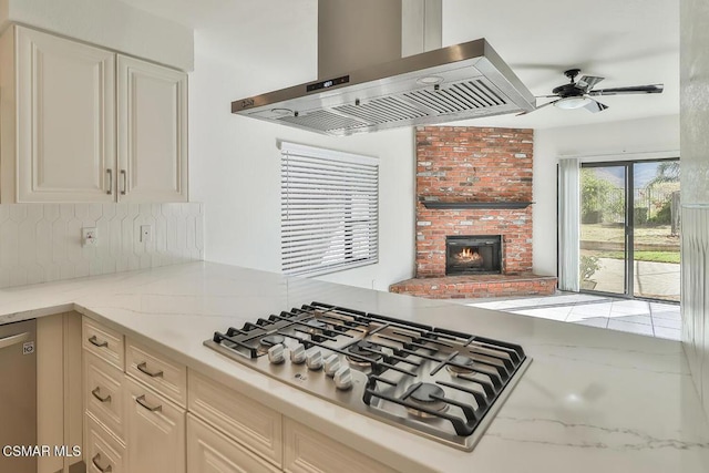 kitchen featuring light stone counters, a brick fireplace, stainless steel appliances, and island exhaust hood