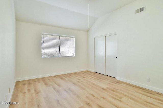 unfurnished bedroom featuring vaulted ceiling, light hardwood / wood-style floors, and a closet