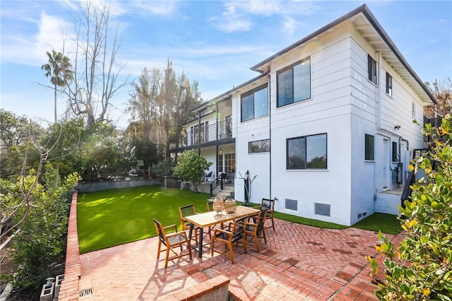 back of property featuring a balcony, a patio area, and a lawn