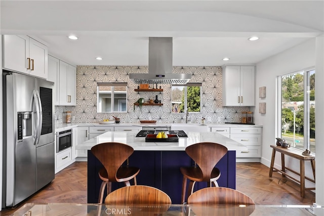 kitchen featuring a kitchen island, appliances with stainless steel finishes, island range hood, parquet flooring, and white cabinets