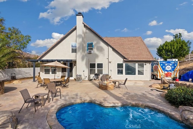 rear view of property featuring a fenced in pool, a patio area, and a fire pit