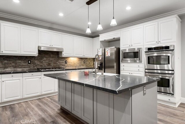 kitchen with appliances with stainless steel finishes, white cabinetry, backsplash, a center island with sink, and light wood-type flooring