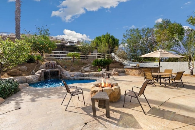 view of swimming pool featuring pool water feature, an outdoor kitchen, an outdoor fire pit, and a patio