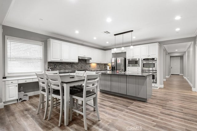 kitchen featuring a kitchen island, appliances with stainless steel finishes, white cabinets, hanging light fixtures, and light hardwood / wood-style floors