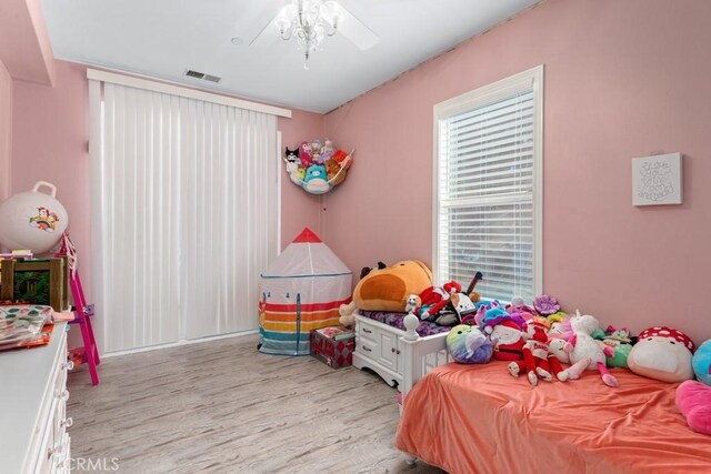 bedroom with ceiling fan with notable chandelier and light hardwood / wood-style flooring