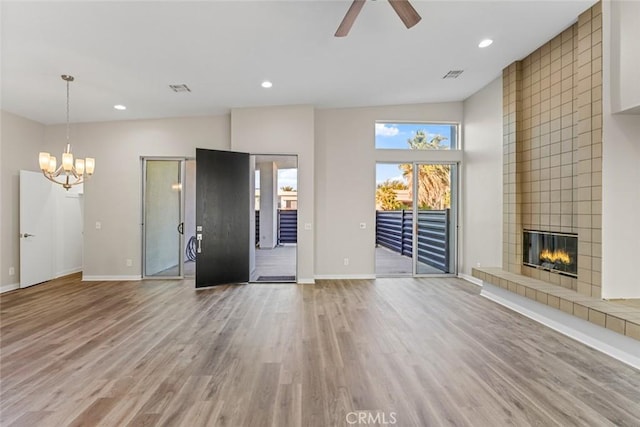 unfurnished living room with a tiled fireplace, ceiling fan with notable chandelier, and wood-type flooring