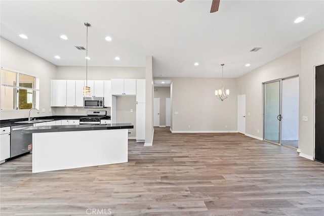 kitchen with white cabinets, hanging light fixtures, a center island, stainless steel appliances, and light wood-type flooring